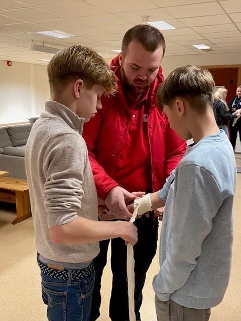 to ungdommer øver på å stoppe blødning med bandasje, sammen med instruktør fra Røde kors - Klikk for stort bilde