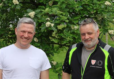 Mads Birk Andersen (fagansvarlig park og grønt) til venstre og Kjetil Jensen (samferdsel) til høyre, stående utendørs med et grønt tre i bakgrunnen.