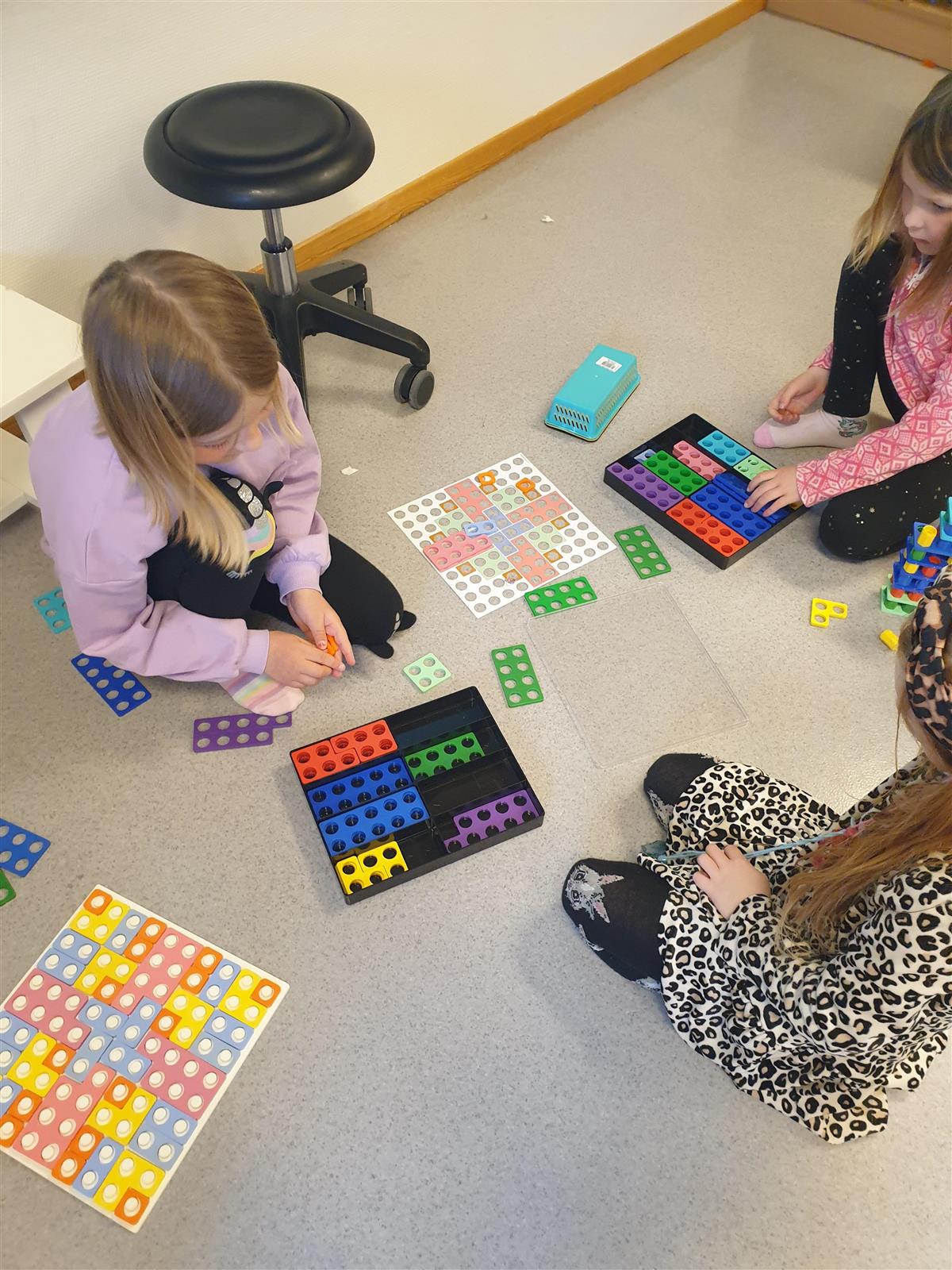 Tre elever som sitter på gulvet og gjør en praktisk matematikkoppgave. - Klikk for stort bilde